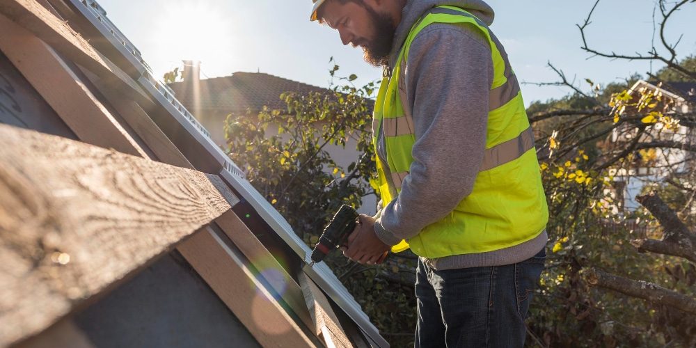 A man using an electric drill to install a new roof, demonstrating professional roof replacement techniques