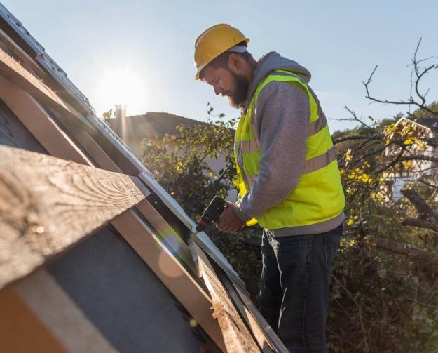 A man using an electric drill to install a new roof, demonstrating professional roof replacement techniques