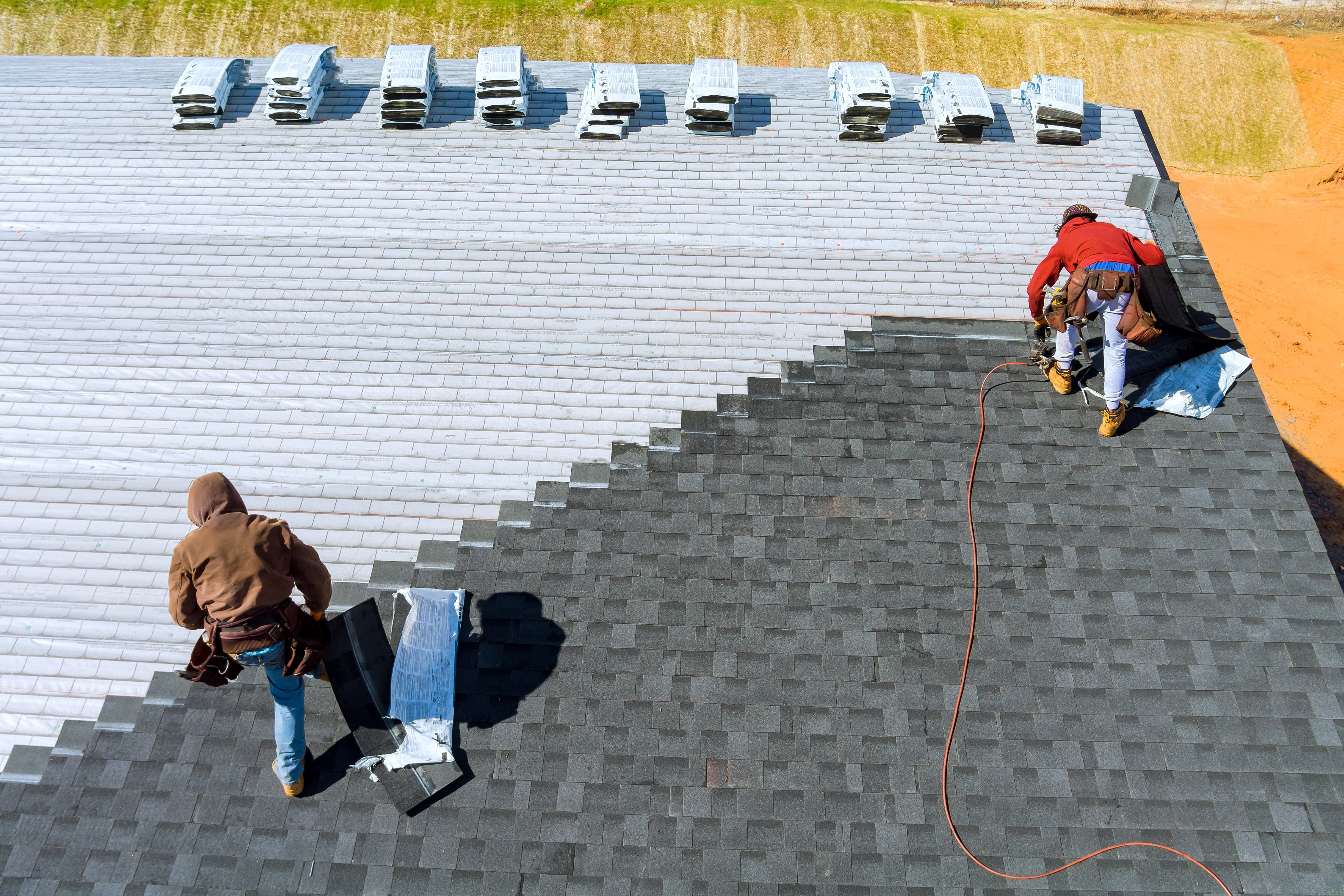 Two professional roofers are seen installing a roof on a house, with one roofer securing shingles and the other managing roofing materials during the roof installation process.