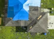 Top view of house with damaged roof, partially covered by blue tarp.