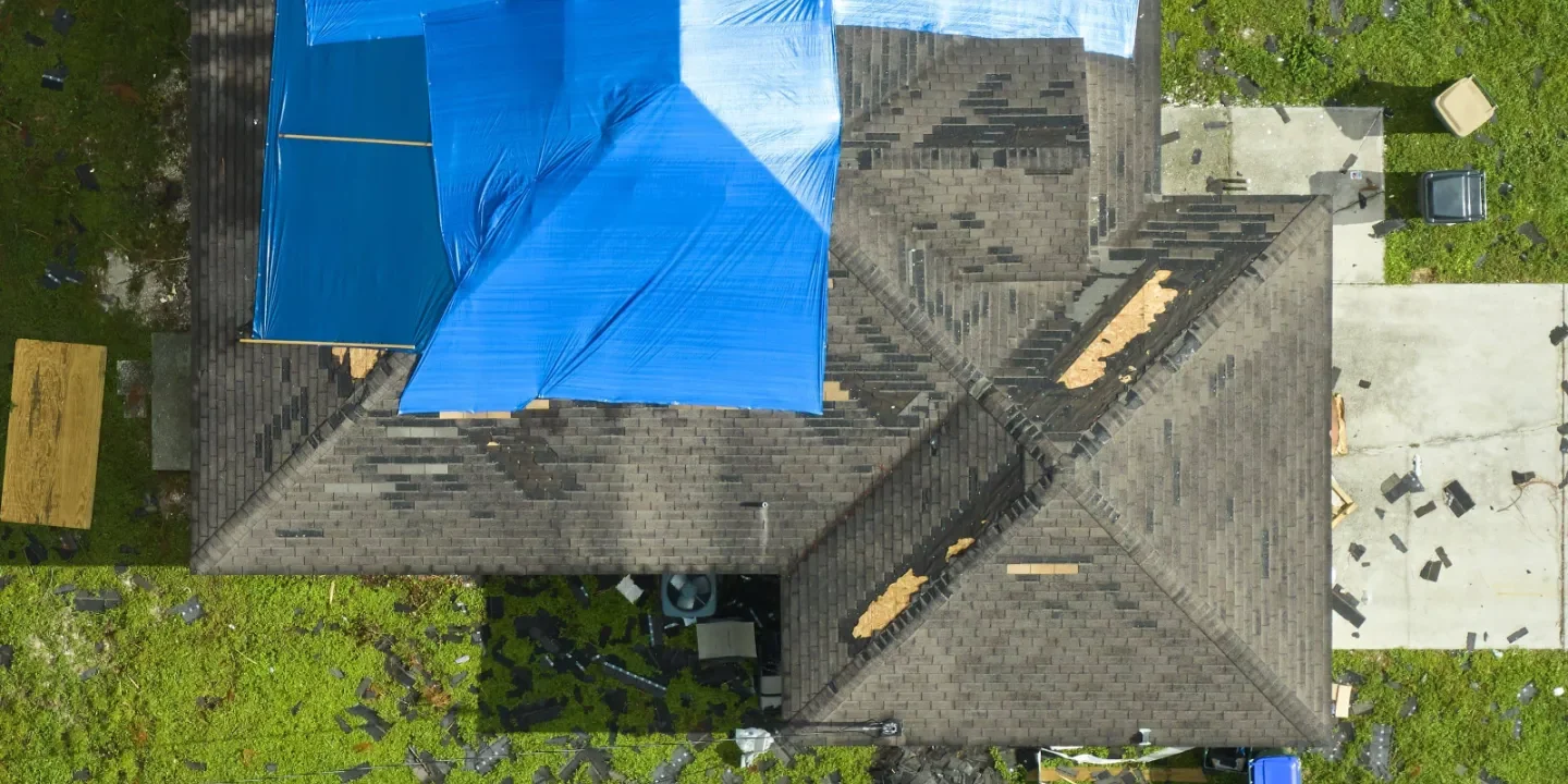 Top view of house with damaged roof, partially covered by blue tarp.