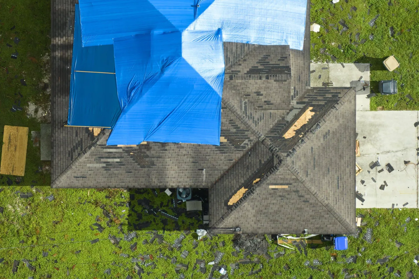 Top view of house with damaged roof, partially covered by blue tarp.